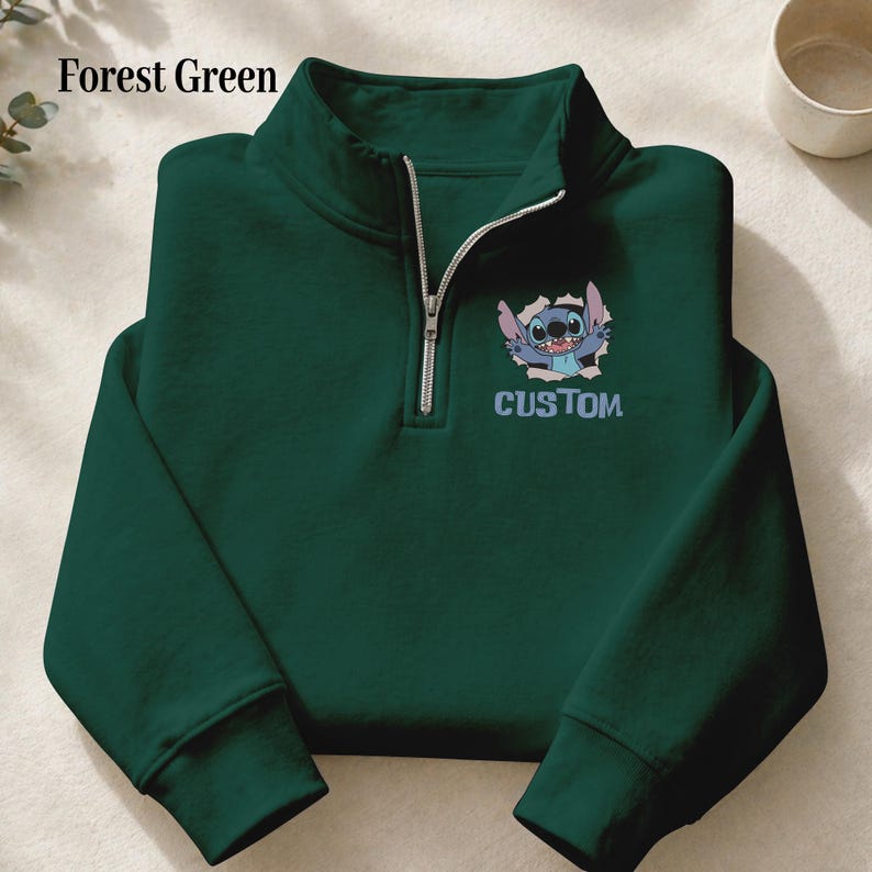 May include: Forest green quarter-zip sweatshirt featuring a cartoon character graphic and the word "CUSTOM". The sweatshirt has a silver zipper and a high collar. The text "Forest Green" is in the upper left corner.