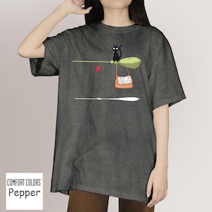 May include: Dark grey t-shirt with a whimsical graphic. A black cat sits on a broom with a sign that reads "NOT IN SERVICE." A red package hangs from the broom. The shirt is labeled "Comfort Colors Pepper."