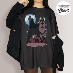 May include: Black Comfort Colors t-shirt featuring a wolf pack graphic. The design includes a large wolf with red eyes, smaller wolves, and a howling wolf in front of a blue moon. The shirt has the words "Comfort Colors Black" in a circle.