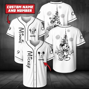 Op de afbeelding: Witte honkbalshirts met zwarte bies, voorzien van Mickey en Minnie Mouse afbeeldingen, kasteelillustraties en vuurwerk. De shirts bevatten de tekst "Minnie" of "Mickey" en "NAME" met een rood kader met "CUSTOM NAME AND NUMBER".
