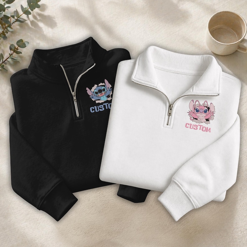 May include: Two pullover sweatshirts, one black and one white, with a quarter-zip collar. Each sweatshirt features a cartoon character graphic and the word "CUSTOM" printed below. The black sweatshirt has a blue and white character, while the white one has a pink character.