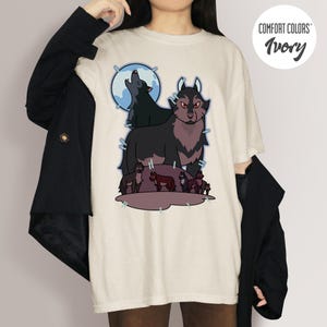 May include: Ivory-colored t-shirt featuring a wolf pack illustration. The design includes a large wolf with red eyes, a howling wolf in front of a blue moon, and several smaller wolves. The shirt has the text "COMFORT COLORS" and "Ivory".