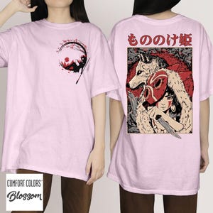 May include: Light pink t-shirts with graphic designs. One shirt features a circular design with a figure reading under a tree. The other shirt displays a character with a wolf and text in Japanese.