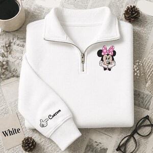 Pode incluir: Camisola branca com gola com fecho de correr e um gr&aacute;fico da Minnie Mouse no peito. A manga apresenta um design personalizado com uma m&atilde;o e a palavra "Custom". A palavra "White" est&aacute; impressa num cart&atilde;o.