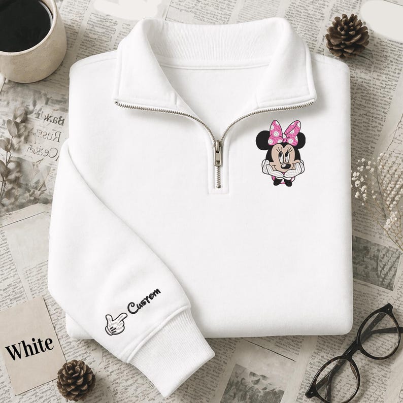 Pode incluir: Camisola branca com gola com fecho de correr e um gr&aacute;fico da Minnie Mouse no peito. A manga apresenta um design personalizado com uma m&atilde;o e a palavra "Custom". A palavra "White" est&aacute; impressa num cart&atilde;o.