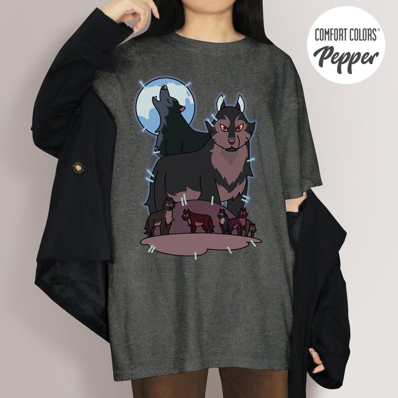 May include: Dark gray t-shirt featuring a wolf pack graphic. The design includes a large wolf with red eyes, a howling wolf in front of a blue moon, and several smaller wolves. The shirt has the text "COMFORT COLORS Pepper".