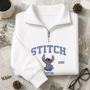 Pu&ograve; includere: Felpa bianca con zip a un quarto di collo con grafica blu di Stitch e la scritta "STITCH" in blu. La felpa ha una chiusura con zip e polsini a coste. Anche l'anno "2002" &egrave; stampato.
