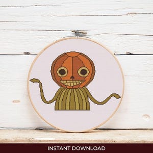 Puede incluir: Un diseño de punto de cruz de un personaje con cabeza de calabaza con una cara sonriente, ojos marrones y brazos extendidos. El diseño está enmarcado en un aro de bordado de madera. El texto "INSTANT DOWNLOAD" está en la parte inferior.