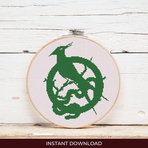 May include: A green cross-stitch design featuring a bird perched on a wheel-like structure, set against a white background. The design is framed in a wooden embroidery hoop. The words "INSTANT DOWNLOAD" are at the bottom.