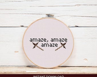 May include: A cross-stitch embroidery hoop with the word "amaze" repeated three times, with two crossed needle designs. The text and designs are in brown thread on a white fabric. The wooden hoop is round. The words "INSTANT DOWNLOAD" are at the bottom.
