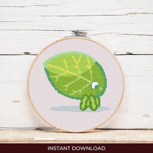 May include: A cross-stitch design of a green leaf with yellow veins, set in a wooden embroidery hoop. The leaf has a cartoon-like appearance. The words "INSTANT DOWNLOAD" are at the bottom.