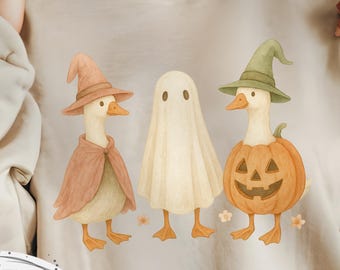 May include: Beige sweatshirt featuring a whimsical Halloween design. The graphic depicts three ducks dressed in costumes: a witch, a ghost, and a jack-o'-lantern. The words "Digital Download" are in a circle at the bottom.