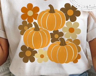 Op de afbeelding: Crèmekleurig T-shirt met een retro ontwerp van drie oranje pompoenen en diverse bruine en gele bloemen. De woorden "Digital Download" staan in een cirkel aan de rechterkant van het shirt.
