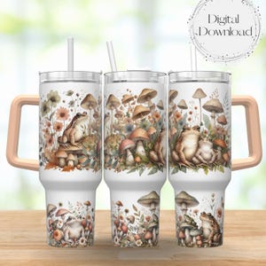 May include: Three white stainless steel tumblers with a pink handle. Each tumbler features a different design of frogs and mushrooms in a forest setting. The tumblers are on a wooden surface.