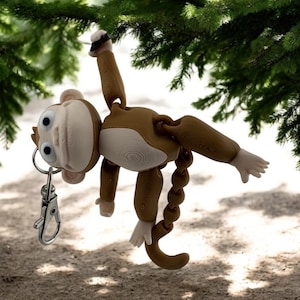 May include: A brown monkey keychain with a silver swivel clasp. The monkey is hanging upside down from a tree branch.