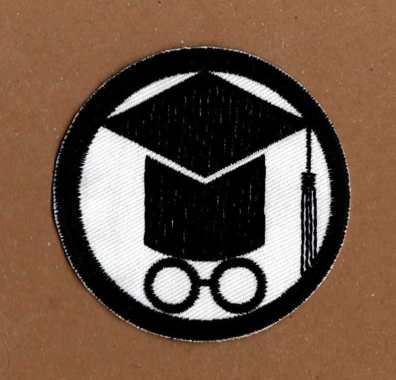 Op de afbeelding: Zwart-witte geborduurde patch met een afstudeerhoed en een bril. De hoed heeft een kwast en de bril is rond.