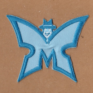 May include: A blue butterfly-shaped patch with a stylized figure wearing a hat and a suit in the center. The figure is outlined in white and the butterfly wings are outlined in blue.