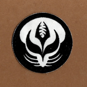 Könnte beinhalten: Schwarz-weiß gestickter Aufnäher mit einem stilisierten Blumendesign. Die Blume hat eine zentrale Knospe und Blütenblätter, die sich nach außen erstrecken.