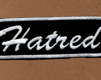 May include: Black and white embroidered patch with the word "Hatred" in a white cursive font.