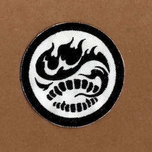 May include: Black and white embroidered patch featuring a stylised scorpion design. The scorpion is curled up with its tail raised. The patch is circular and has a black border.