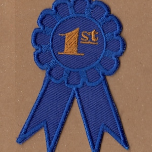 May include: A blue ribbon with a gold embroidered "1st" in the center. The ribbon is tied in a bow and has a scalloped edge.
