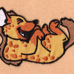 May include: A brown and yellow embroidered patch of a laughing hyena with a white ear.