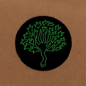 May include: A black embroidered patch featuring a green tree design. The tree has a snake-like trunk and branches with leaves.