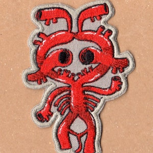 May include: Red embroidered iron-on patch of a cartoon creature with a large head, two eyes, and a body with multiple limbs. The creature is standing with its arms raised.