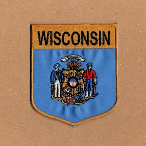 May include: A blue and gold embroidered patch with the word "WISCONSIN" in black lettering. The patch features the state seal of Wisconsin, which includes a shield with a red, white, and blue design, two figures holding tools, and the word "FORWARD" above the shield.