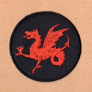 May include: A red embroidered dragon patch on a black circular background. The dragon is facing right and has its wings spread out.