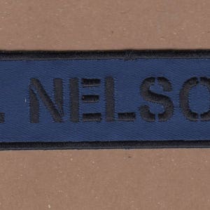 May include: A blue name tag with black stitching around the edges. The name "M. NELSON" is printed in black letters.