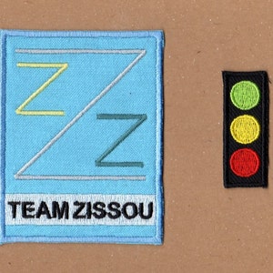 May include: Two embroidered patches. The first patch is blue with a white border and the text "TEAM ZISSOOU". The second patch is black with a red, yellow, and green traffic light.
