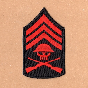 May include: A black embroidered patch with three red chevrons, a red skull and crossbones, and a red helmet. The patch is shaped like a chevron.