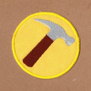 Peut inclure: Un cercle jaune avec une bordure jaune, représentant un marteau brun et gris.