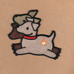 Puede incluir: Parche bordado de un perro marrón y beige con un collar rojo y una pequeña llama naranja en su costado. El perro está corriendo y tiene una oreja marrón que sobresale de debajo de su cabeza.