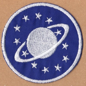 May include: A blue and white embroidered patch with a white planet and ring design surrounded by white stars.