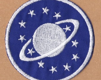 May include: A blue and white embroidered patch with a white planet and ring design surrounded by white stars.