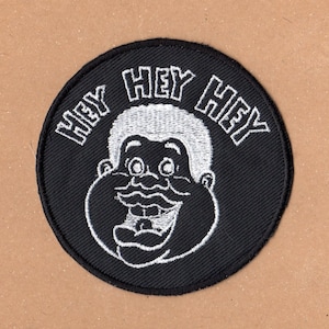 May include: Black and white embroidered patch featuring a cartoon character's face and the text "Hey Hey Hey" around the edge.