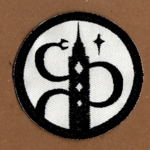 May include: Round patch with a black border and a white interior. The design shows a black tower with diamond shapes, a star, and a curved shape like the letters 'C' and 'D'.