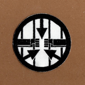 May include: Black and white embroidered patch with a circular design. The centre of the circle has a white background with four black arrows pointing inwards. The arrows are surrounded by a black circle with a white border.