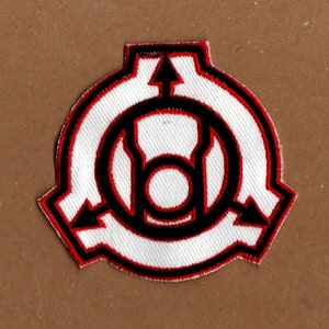 May include: A white embroidered patch with a black and red outline. The patch features a stylised symbol with arrows pointing in opposite directions and a circle in the centre.