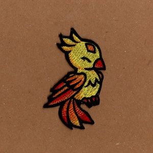 May include: An embroidered bird patch in yellow and orange with a red beak. The bird is facing to the right and has its wings spread out.