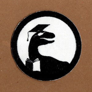 May include: Black and white embroidered patch of a dinosaur wearing a graduation cap. The dinosaur is facing right and has a long neck and tail.