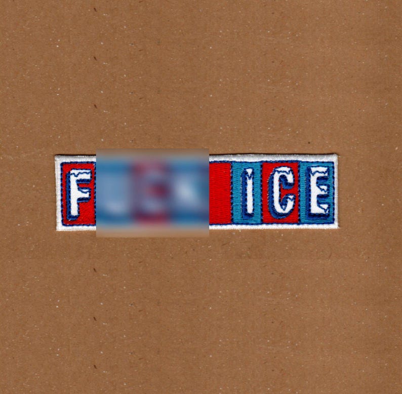 May include: Embroidered patch with the word "ICE" in white letters, with a red and blue color scheme. The first part of the word is blurred out. The patch is rectangular with a white border, set against a brown background.
