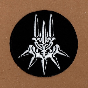 May include: A black and white embroidered patch with a stylized design of a crown with spikes. The patch is circular and has a black background.