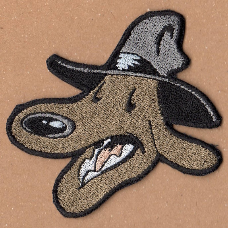 Pu&ograve; includere: Toppa ricamata di un cane dei cartoni animati che indossa un cappello. Il cane ha un corpo marrone e nero, un naso nero e una bocca bianca con i denti. Il cappello &egrave; grigio con un bordo nero.
