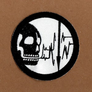 May include: Black and white embroidered patch with a skull and a heart rate line. The patch is circular and has a black border.