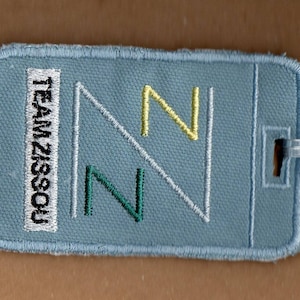 Puede incluir: Una insignia de tela azul con costuras blancas y el texto "TEAM 21SSOU" en blanco. La insignia tiene una "N" blanca y amarilla y una "N" verde bordadas.