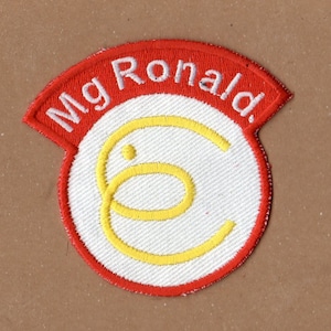 May include: A red and white embroidered patch with the text "Mg Ronald" in white lettering on a red background. The patch features a white circle with a yellow double-C logo in the center.