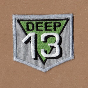 May include: A gray and green embroidered patch with the text "DEEP 13" in a triangular shape.